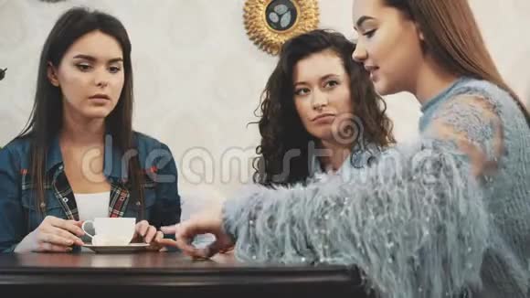 三个好的年轻女朋友在一家咖啡馆相遇同时喝卡布奇诺有长长的黑发视频的预览图