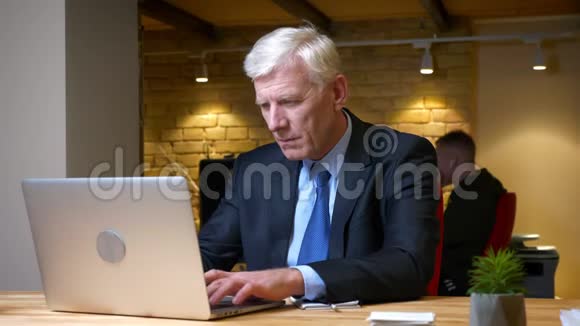 在办公室工作的白种人老商人在笔记本电脑上做笔记的特写镜头视频的预览图