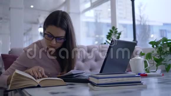在线课程学生女孩在笔记本上写笔记看书坐在桌上用笔记本电脑视频的预览图