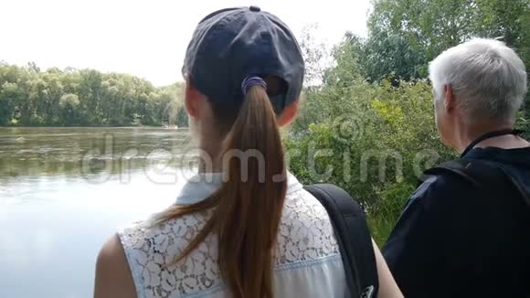 快乐旅行的概念男人和女孩一起远足带背包的徒步旅行者他们停在河岸上看着它视频的预览图