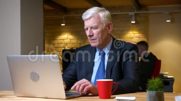 在办公室里用笔记本电脑和在室内喝咖啡的老白种人员工的特写镜头视频的预览图