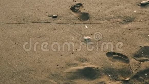 海浪翻滚上岸人类脚印在沙滩上特写日出或日落时间低角度视角慢镜头视频的预览图