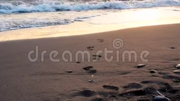 海浪翻滚上岸人类脚印在沙滩上特写日出或日落时间低角度视角慢镜头视频的预览图