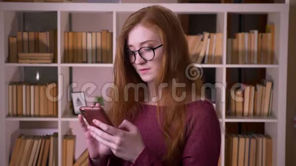 在大学里戴着眼镜的年轻红发美女戴着眼镜在电话里发短信视频的预览图
