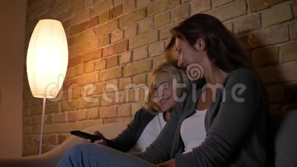年轻的白种人女性和她的小女儿在电视上看节目并使用遥控器进行特写拍摄视频的预览图