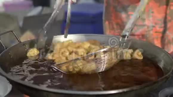 小贩正在平底锅里拣许多油炸面粉油炸面团粘在鼓泡油里视频的预览图