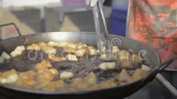 小贩正在平底锅里煎许多面粉油炸面团粘在鼓泡油里视频的预览图