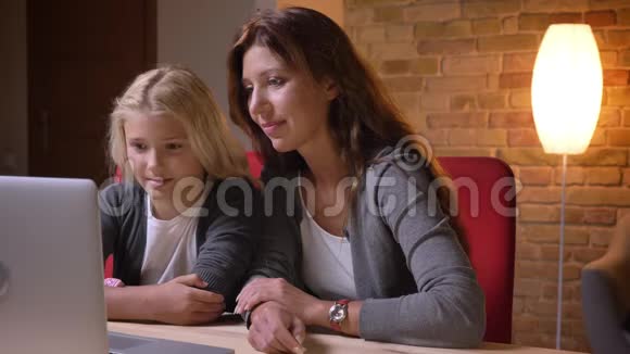 一个年轻的白种人女人和她的小漂亮女孩在笔记本电脑上看视频笑着玩着视频的预览图