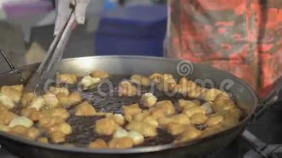 小贩正在平底锅里煎许多面粉油炸面团粘在鼓泡油里视频的预览图