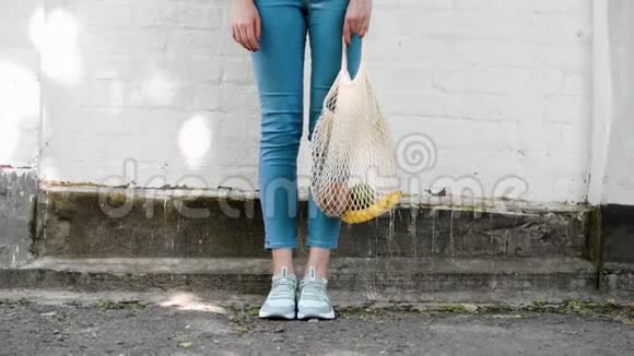 女孩双腿可重复使用网绳编织购物袋与水果和蔬菜移动视频的预览图