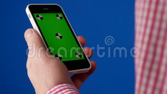 男人手拿着智能手机在一个垂直的位置并作出触摸手势手机上的绿色屏幕和蓝色视频的预览图
