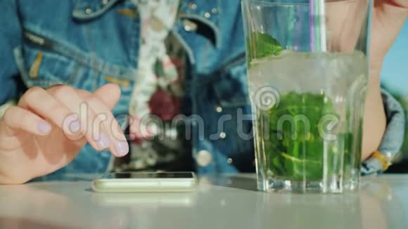 女性手在智能手机屏幕上翻转信息附近有一个装有鸡尾酒的玻璃杯视频的预览图