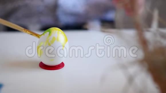 一个小孩子用画笔在桌子上的一个支架上涂上黄色的复活节彩蛋视频的预览图