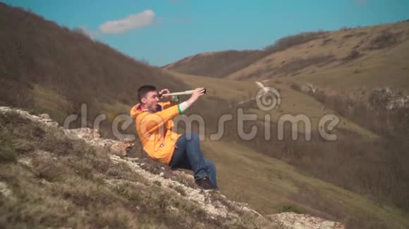 一个穿着黄色夹克蓝色牛仔裤的年轻人坐在岩石上透过一把望远镜透过望远镜视频的预览图