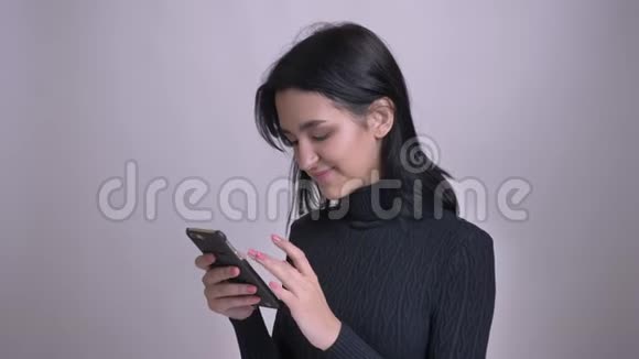 一位年轻迷人的白种人女性用手机上网然后看着摄像机微笑着进行特写拍摄视频的预览图