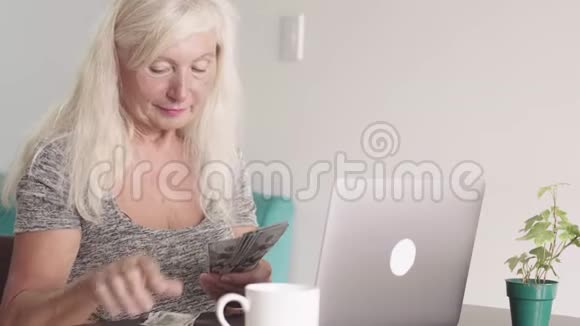 在家里坐在笔记本电脑前祖母数着一捆钱视频的预览图