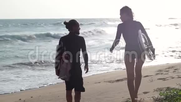 日落时分两个年轻人正拿着冲浪板在海滩上散步视频的预览图
