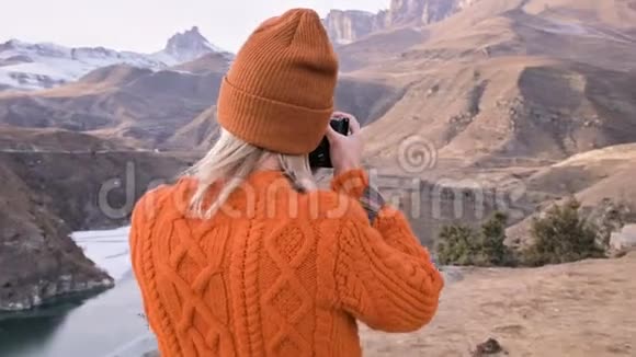 后景女孩摄影师旅行者穿着橙色毛衣和帽子在他的dslr相机景观上拍照视频的预览图