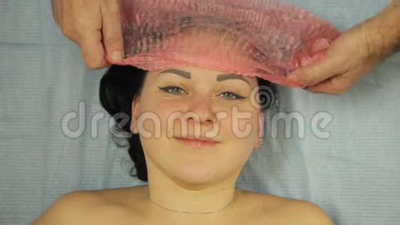 戴手套的美容师把一顶化妆帽戴在女人头上视频的预览图