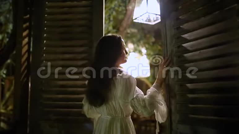 一个穿着老式白裙的漂亮女孩打开了通往露台的门视频的预览图