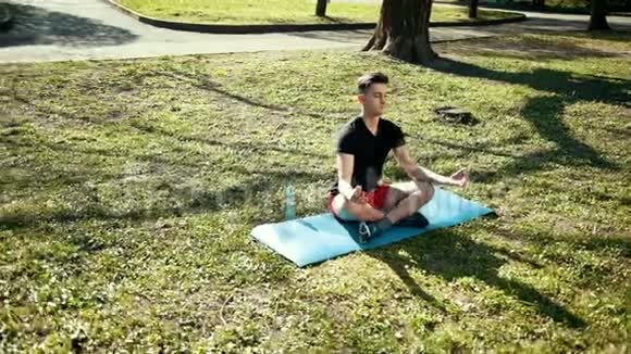 公园里的瑜伽在莲花位置的年轻人坐在绿草上和平与冥想的概念专业慢视频的预览图