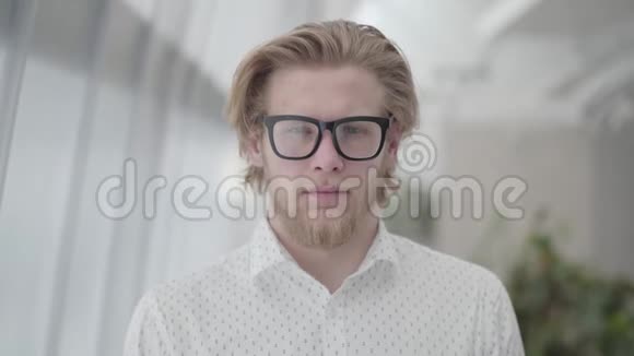 肖像成功的金发男子戴着眼镜站在一间光线舒适的办公室里看着相机帅哥视频的预览图