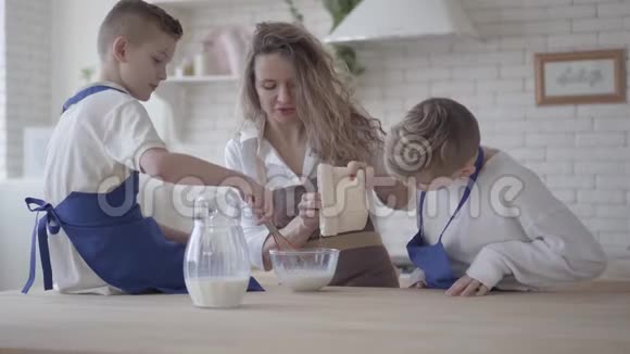 漂亮的女人和她的两个儿子在厨房里做面团男孩们帮助母亲做食物妈妈来了视频的预览图