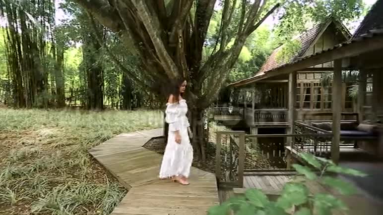 一个穿着白色衣服的年轻女子走在通往房子的小路上在门口转过身来在背景中有一个热带的前视频的预览图