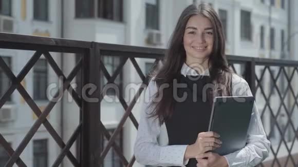 露台上一个漂亮的年轻女人的肖像看着相机手里拿着笔记本电脑女商人的支出视频的预览图