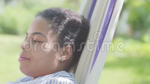 美丽的非裔美国女人躺在吊床上在花园里放松户外休闲令人愉快视频的预览图