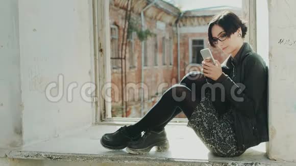 年轻时髦的女人坐在老楼的窗台上使用手机视频的预览图