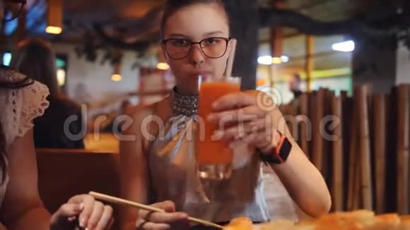 母女俩用木筷卷吃饭少女从杯子里喝新鲜胡萝卜汁视频的预览图