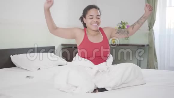 迷人的微笑非洲裔美国妇女刚刚醒来她伸展她的身体举起她的手臂快乐女孩放松视频的预览图