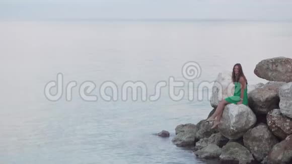 一个女人坐在靠近大海的岩石上视频的预览图