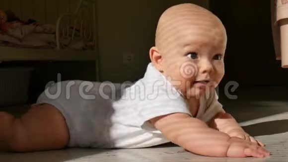 没有头发的幼儿躺在地板上看着摄像机露出了牙齿般的微笑视频的预览图