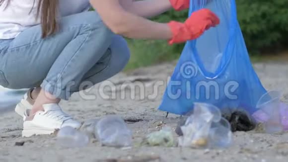爱护自然生态义务女孩戴着橡胶手套在清理海滨时把塑料垃圾收集在垃圾袋里视频的预览图