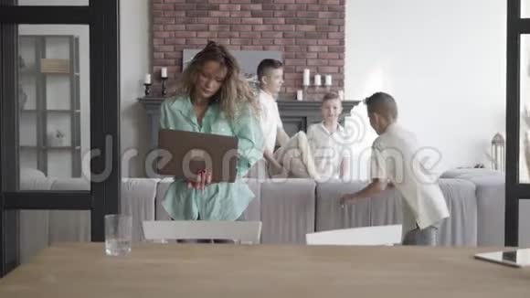 忙碌的母亲在牢房里说话手里拿着一台笔记本电脑站在客房里兄弟俩在愚弄视频的预览图