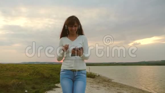 戴着耳机的漂亮女孩带着平板电脑在海滩上散步并且正在在线视频会议快乐的女人在海滩散步视频的预览图