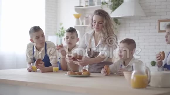 漂亮的快乐女人和她的四个十几岁的儿子站在桌子旁吃着馅饼喝着橙汁视频的预览图