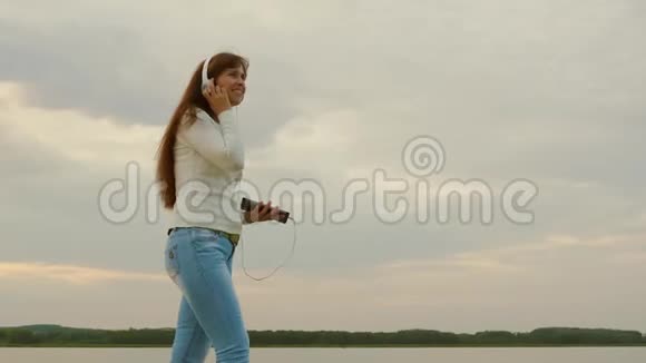 快乐的女人在春天用平板电脑在海滩上散步用耳机听音乐戴耳机的漂亮女孩视频的预览图