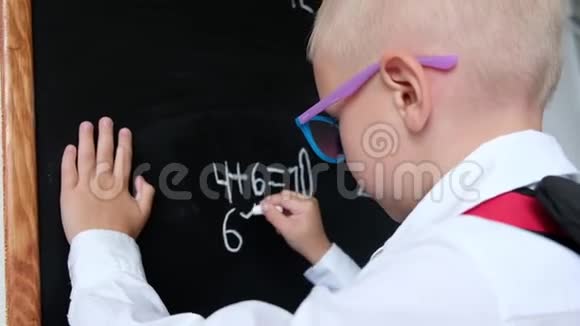 可爱的小男孩在黑板上写字带包的小学孩子教育观念回学校去视频的预览图