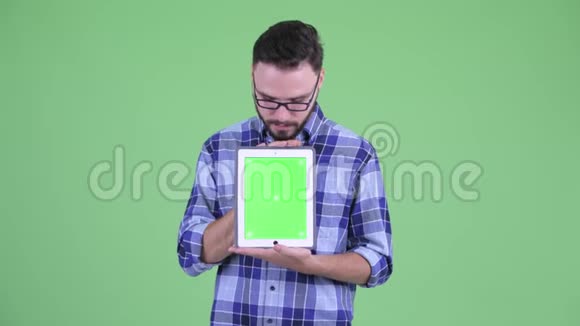 一位年轻快乐的留胡子的嬉皮士展示数码平板电脑看上去很惊讶视频的预览图