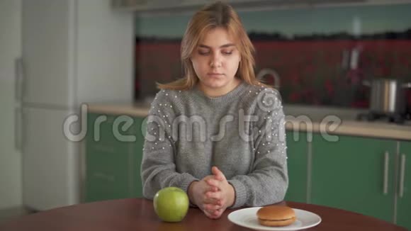一个胖女孩坐在厨房的桌子旁选择健康食物和不健康食物的肖像胖子视频的预览图