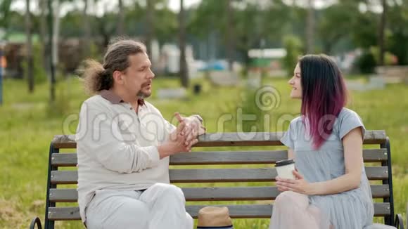 一位轻松迷人的中年男子长发灰白一位染发的年轻女子坐在公园的长凳上视频的预览图