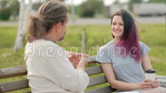 一位轻松迷人的中年男子长发灰白一位染发的年轻女子坐在公园的长凳上视频的预览图