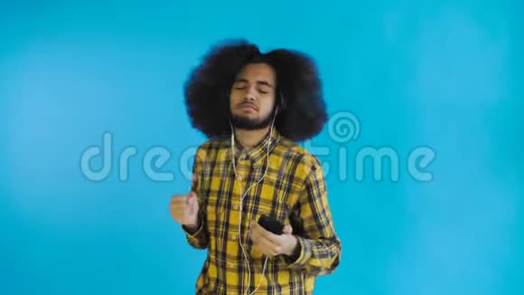 积极的非裔美国人用手机听音乐在他的耳机蓝色背景情感概念视频的预览图