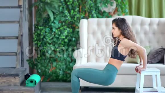 微笑活跃的健身妇女在家中进行锻炼训练用长凳做三头肌锻炼视频的预览图