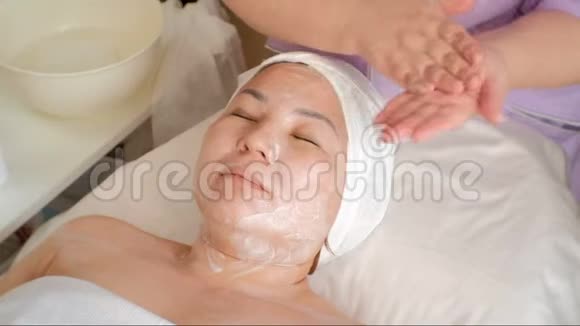 化妆程序一个亚洲女人的特写脸美容师把奶油涂在女性的脖子和肩膀上面对一个视频的预览图