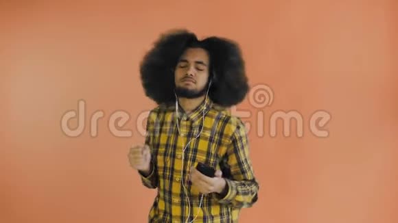 积极的非裔美国人使用电话听音乐在他的耳机橙色背景情感概念视频的预览图