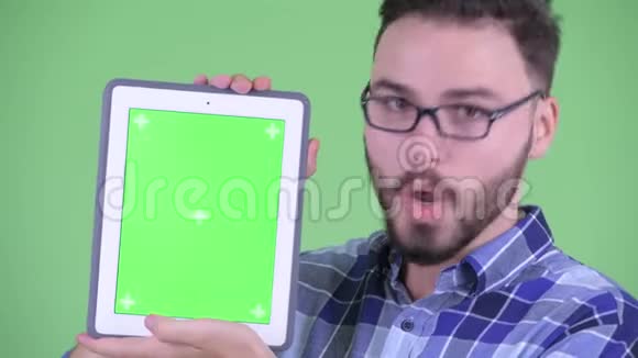 一位年轻快乐的留胡子的嬉皮士展示数码平板电脑看上去很惊讶视频的预览图